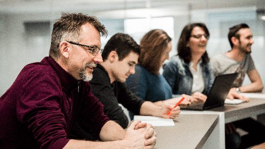 Group of professionals attending a training session or meeting, working on laptops and taking notes in a collaborative learning environment.